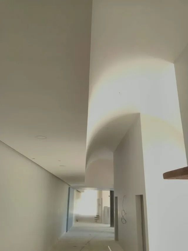 Pasillo luminoso y minimalista, con paredes blancas arqueadas y una puerta al fondo