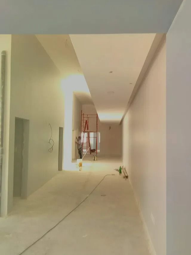 Pasillo estrecho sin terminar, con paredes blancas, suelo de hormigón y materiales de construcción al fondo.