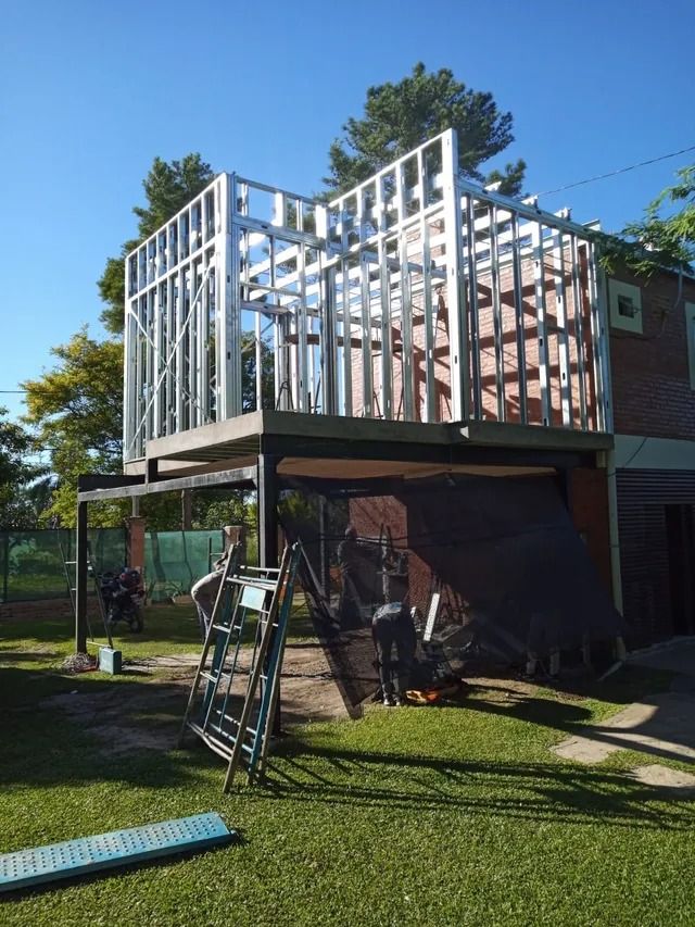 Casa en construcción en el patio trasero, con la estructura de madera expuesta en la planta superior y escaleras debajo