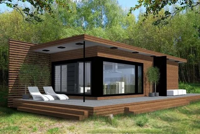 Pequeña casa moderna de madera y color negro, con terraza y tumbonas, en un entorno arbolado y cubierto de césped