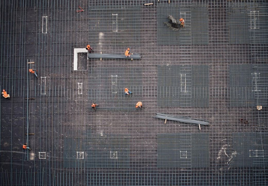 Trabajadores sobre una estructura de barras de acero en una obra, vistos desde arriba.