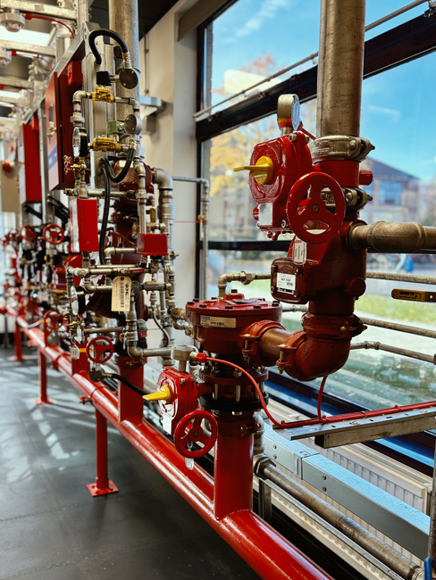 A row of red pipes and valves in a room with a window.