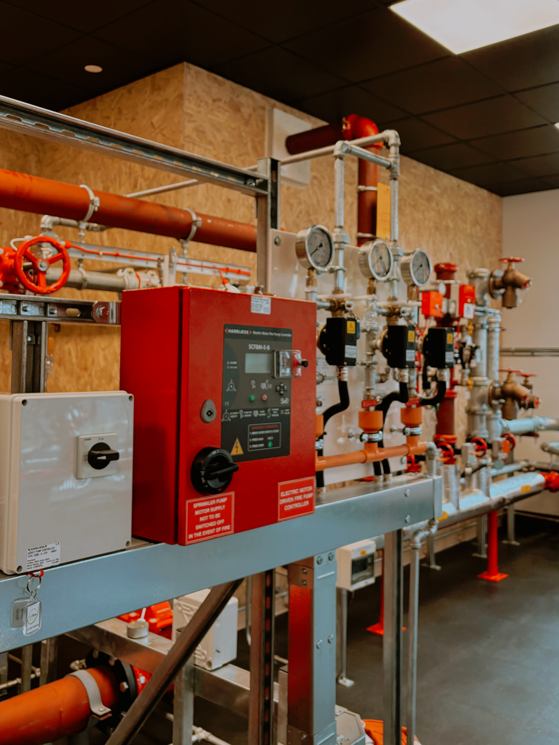 A room with a lot of pipes and a red box on the wall.