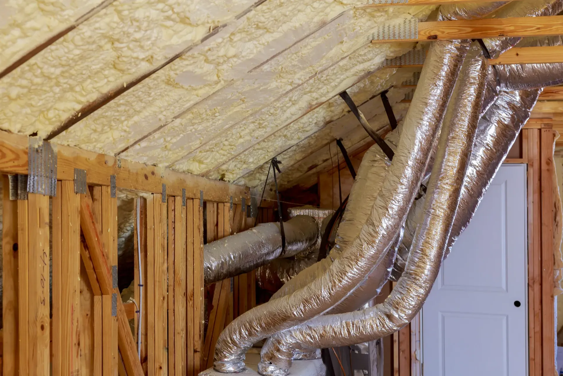 An interior view of a wooden attic frame with foam insulation between beams and a square skylight open to the sky.