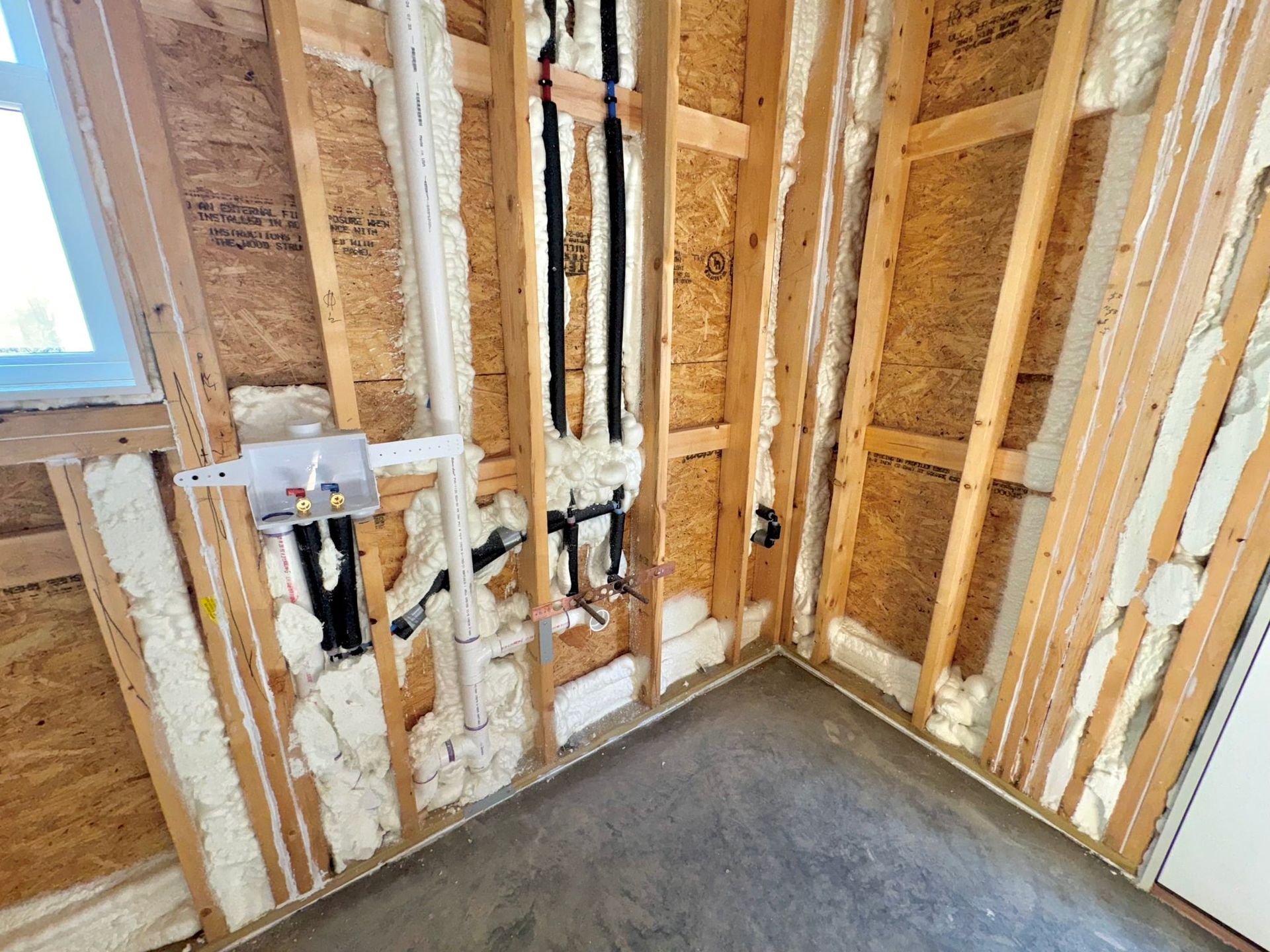 An interior view of a wooden attic frame with foam insulation between beams and a square skylight open to the sky.