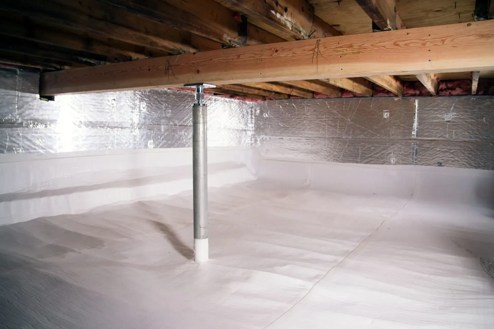 Crawl space with a white vapor barrier, reflective insulation on the foundation walls, and a single metal support column.