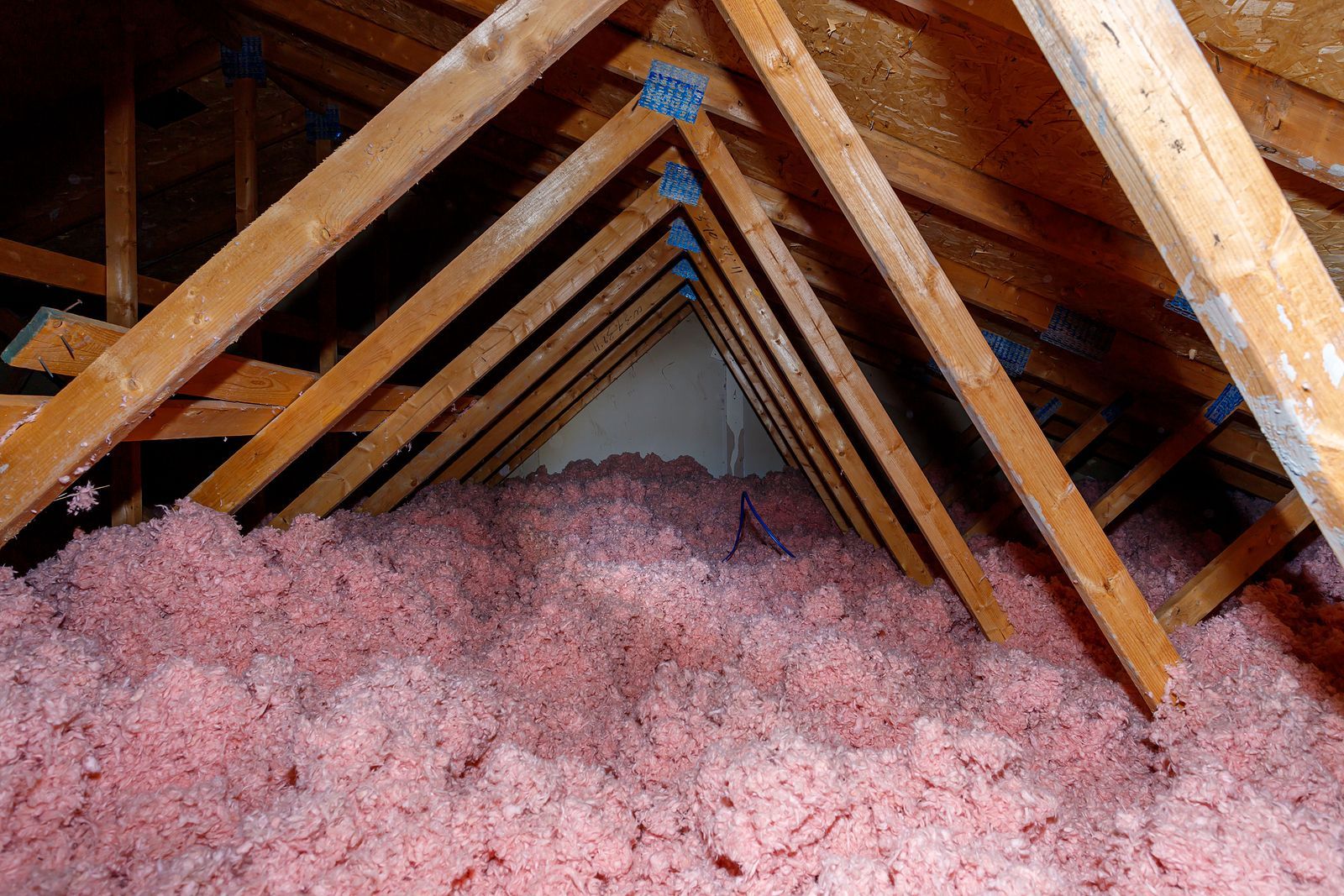 An interior view of a wooden attic frame with foam insulation between beams and a square skylight open to the sky.