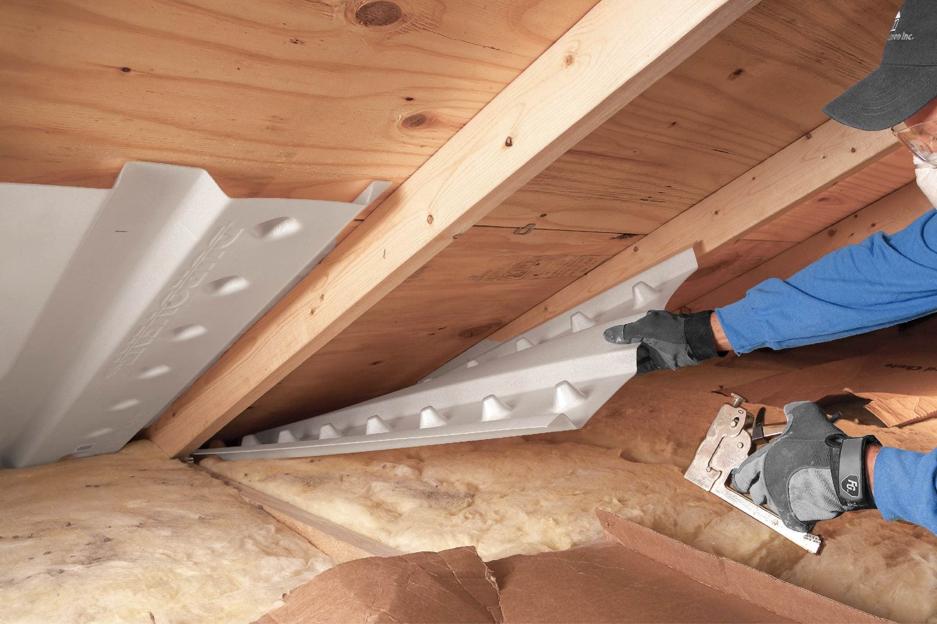 A person in a hard hat standing on a ladder and spraying white foam insulation onto an unfinished interior wall.
