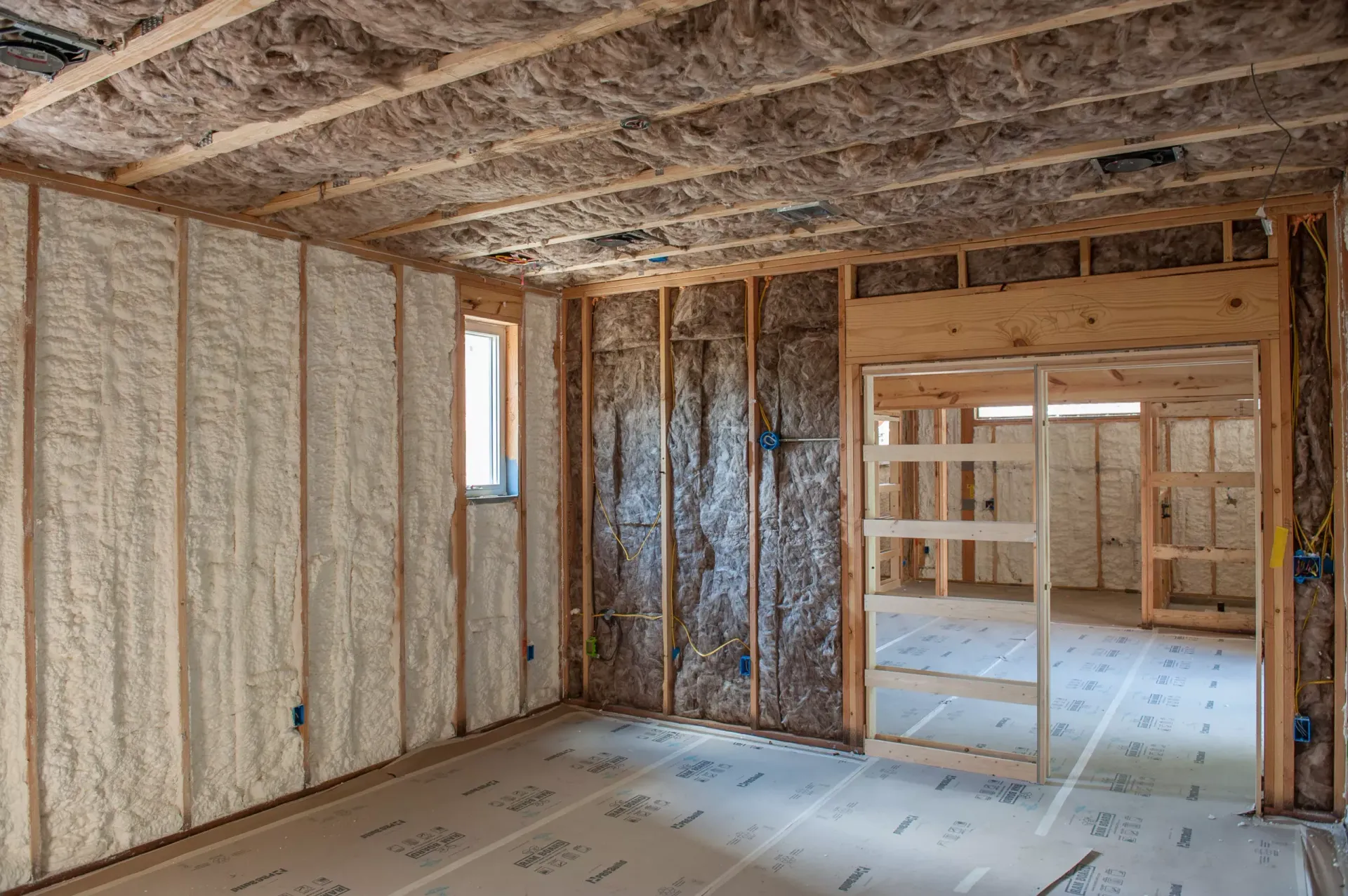 A person in protective gear installs a white vapor barrier against the walls and floor of a crawl space.