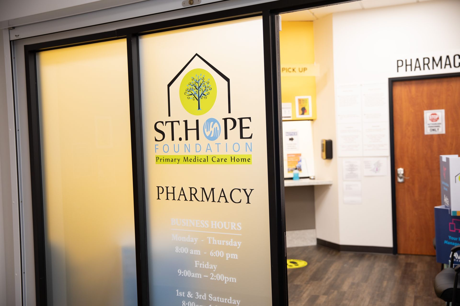 The St. Hope Foundation pharmacy entrance with operating hours listed on a glass sliding door.