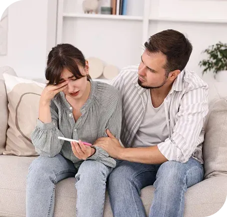 Woman crying, holding a pregnancy test, comforted by a man on a couch.