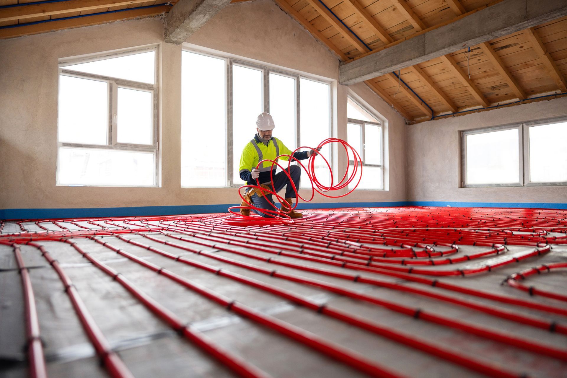 Engineer installing red tubing for underfloor heating system in modern house.