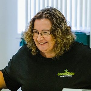 A woman wearing glasses and a black shirt is smiling while sitting at a desk.