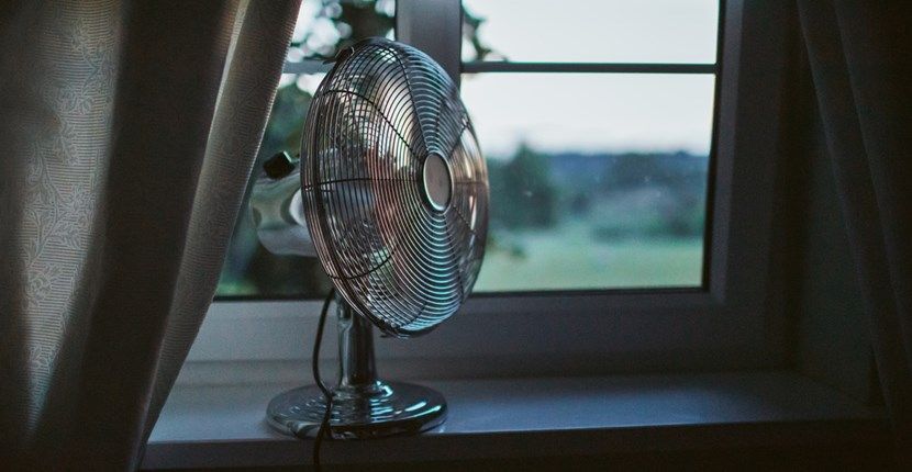 A fan is sitting on a window sill next to a window.
