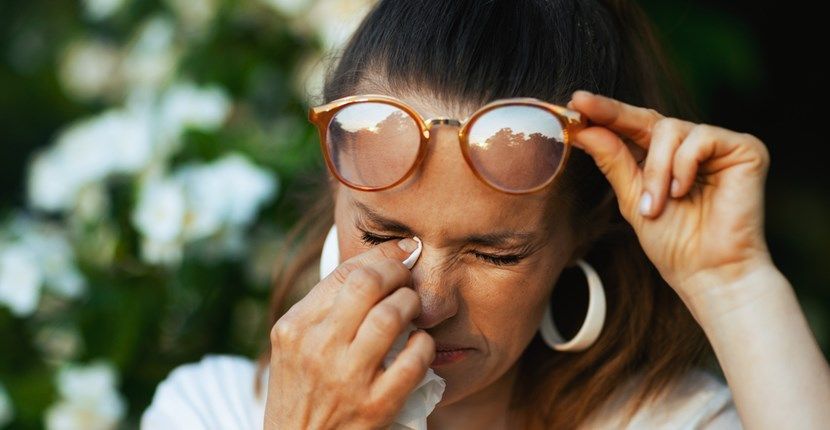A woman wearing sunglasses is cleaning her eyes with a napkin.