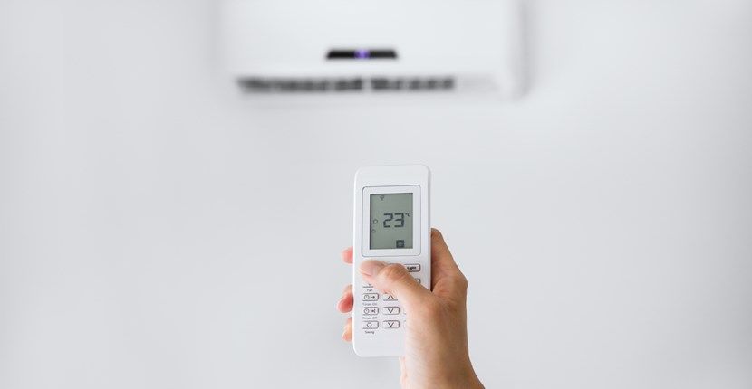 A person is holding a remote control in front of an air conditioner.