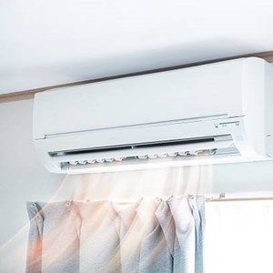 A white air conditioner is hanging from the ceiling in a room next to a window.