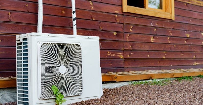 A white air conditioner is sitting on the side of a wooden house.