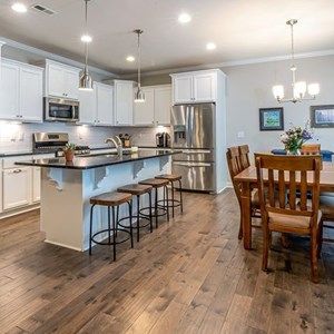 A kitchen with white cabinets , stainless steel appliances , hardwood floors and a large island.
