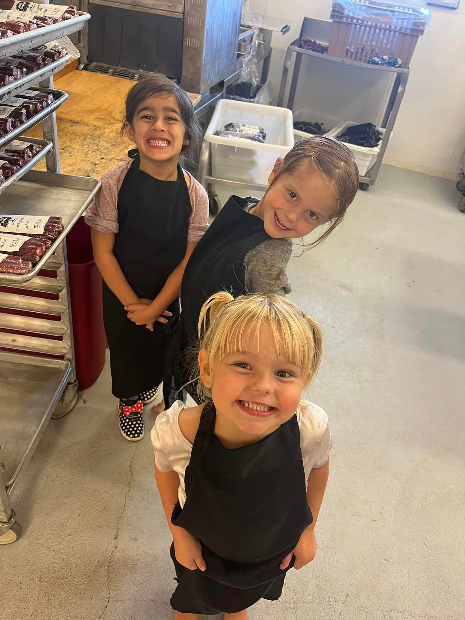 three little girls wearing aprons are posing for a picture in butcher shop