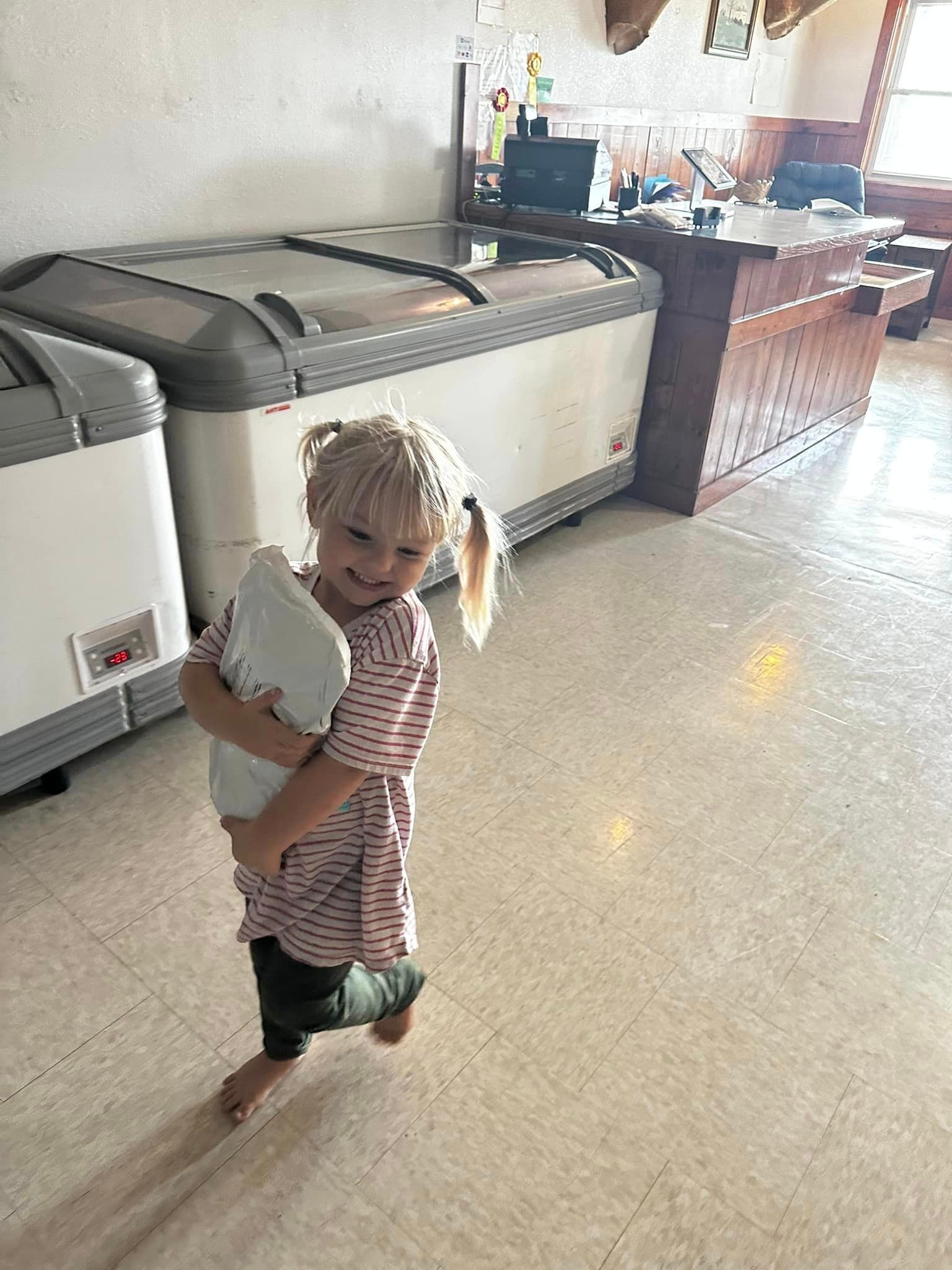 a little girl holding a bag in front of a row of freezers