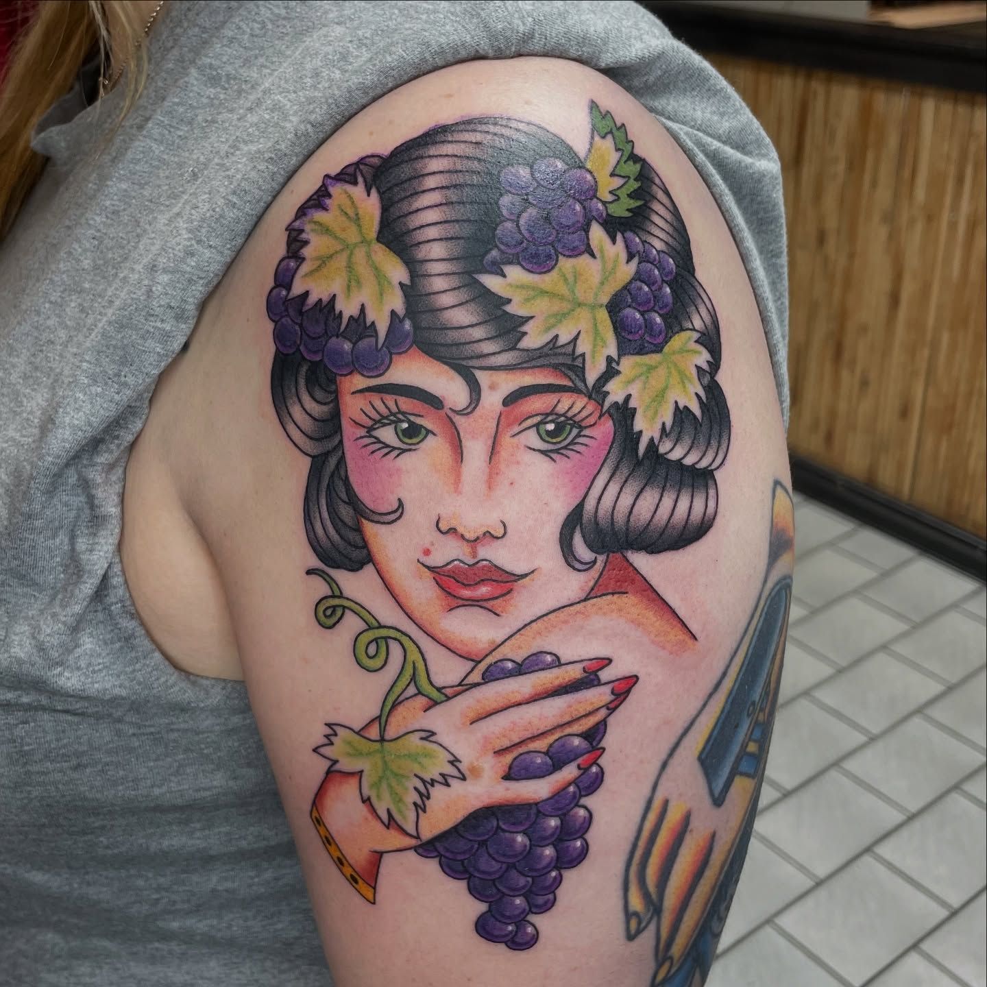 Fargerik old school-tatovering av kvinne med druer og grønne blader på overarmen