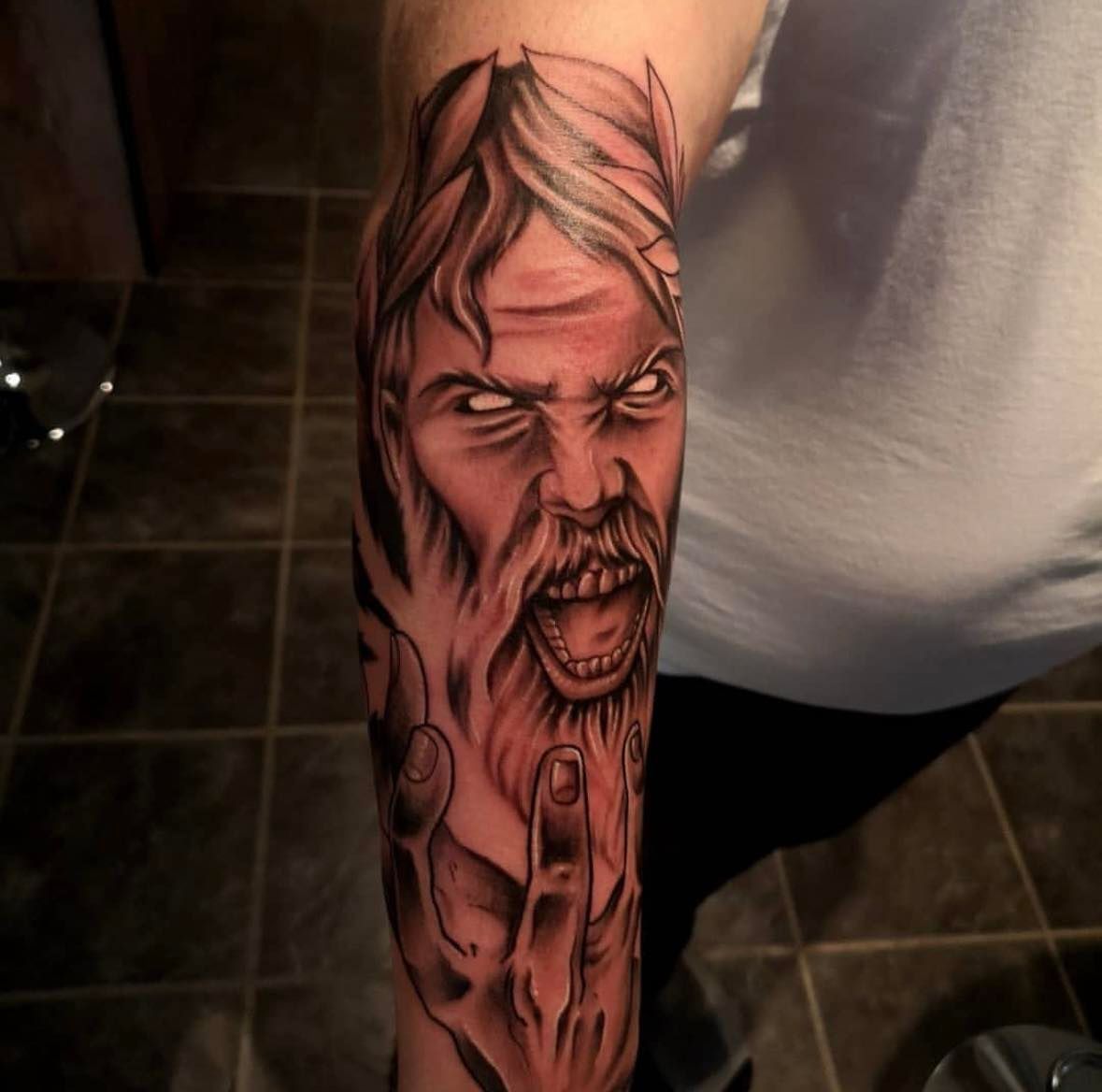 Farget tatovering av aggressiv, skrikende vikingfigur med laurbærblad – på underarm