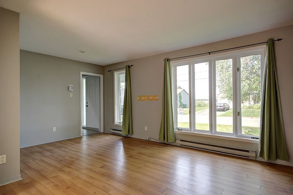 Un salon vide avec du parquet et beaucoup de fenêtres.