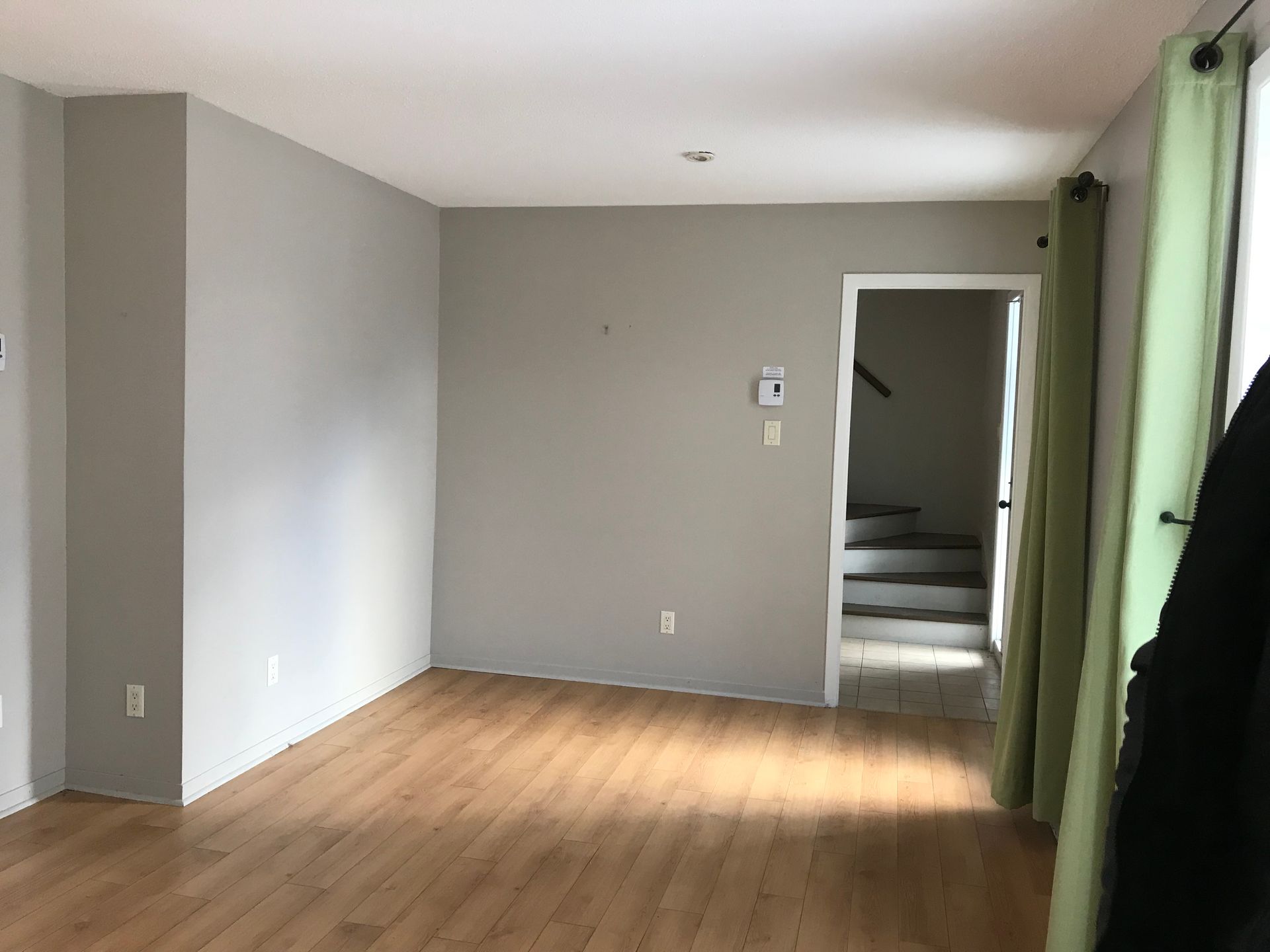 Un salon vide avec du parquet et des escaliers en arrière-plan.