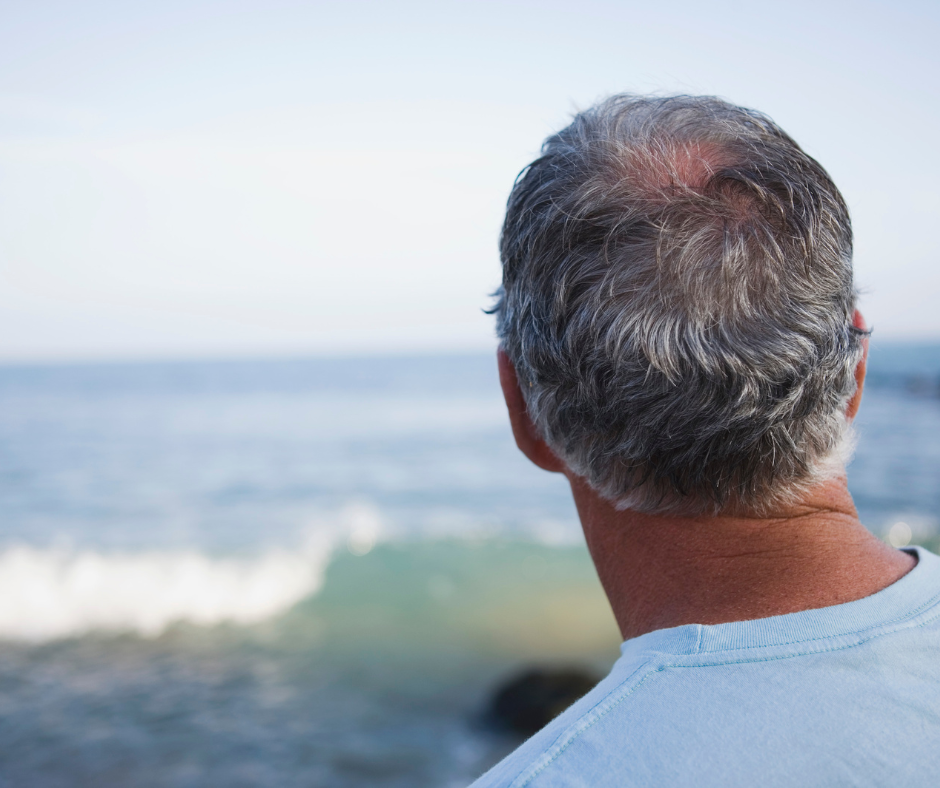 photo of the back of the head of a middle aged man looking out over the ocean