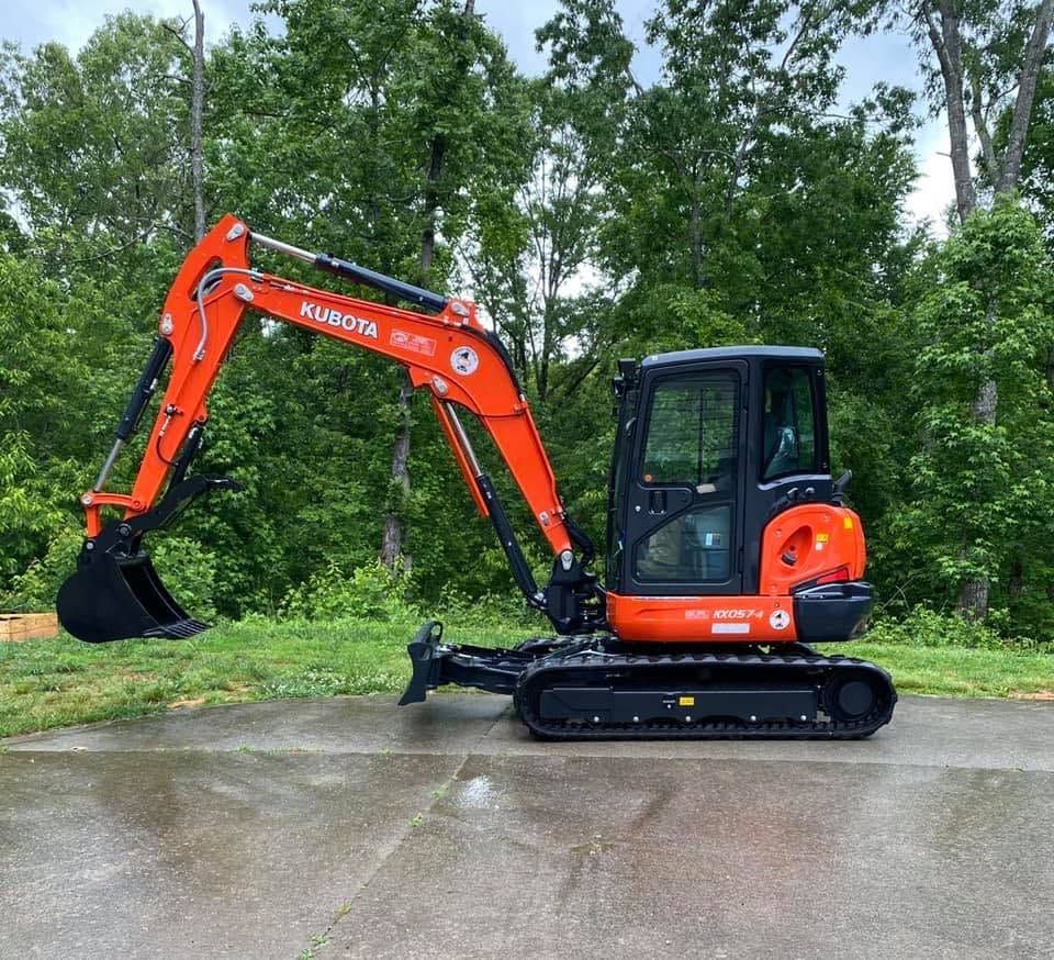 Orange Kubota mini excavator on wet pavement with trees in the background