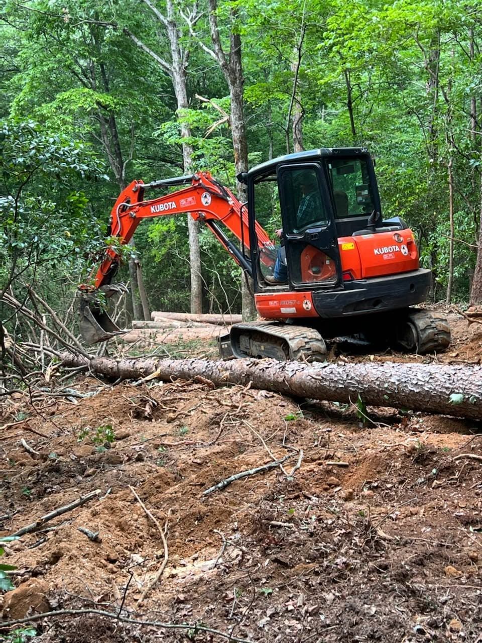 Orange excavator clearing logs in a muddy forest clearing