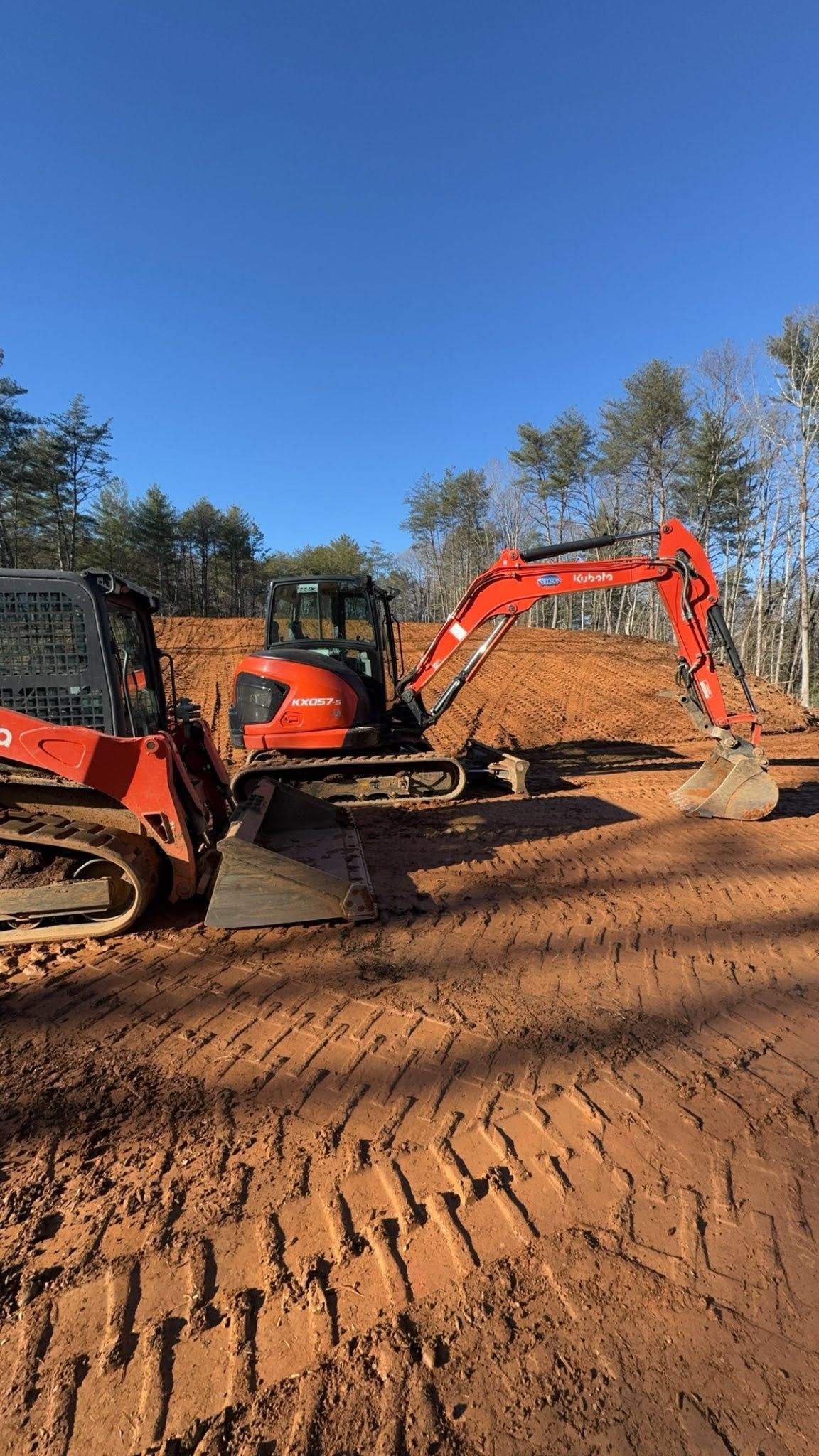 Orange excavator and bulldozer on a dirt construction site under a clear blue sky