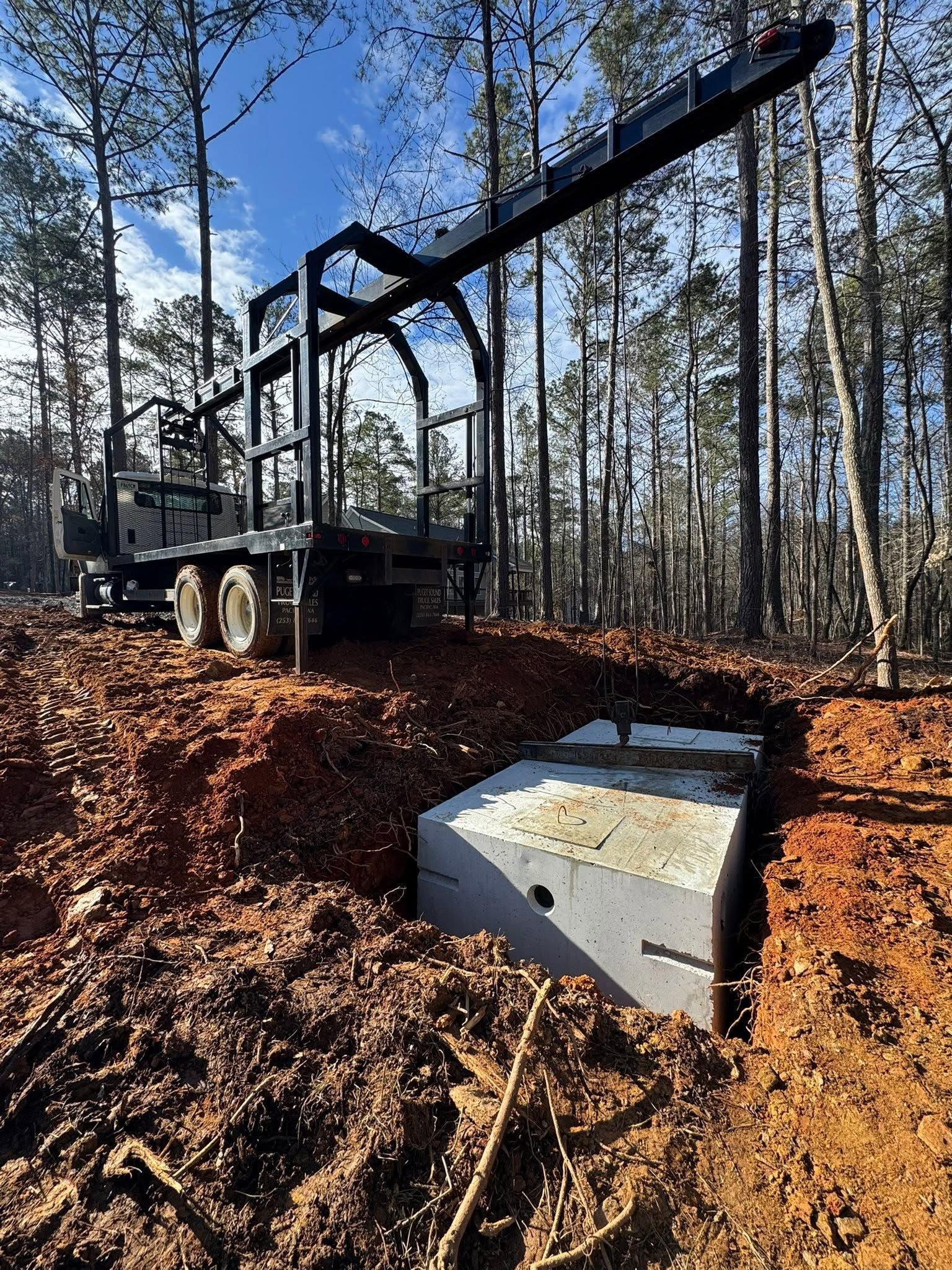 Logging truck beside a concrete culvert in a wooded, muddy clearing