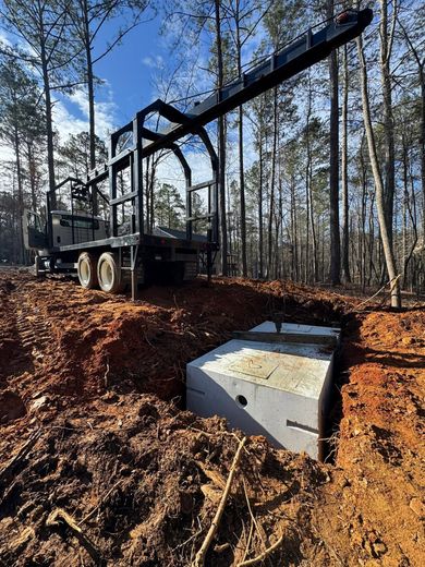 Logging truck beside a concrete culvert in a wooded, muddy clearing
