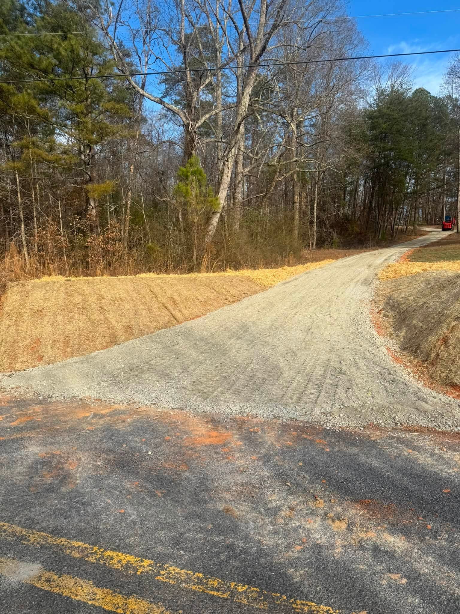 Gravel driveway curving uphill beside winter woods, with road and yellow center lines in the foreground.