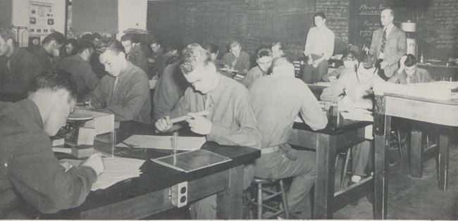 Students seated at desks in a crowded classroom, writing during an exam