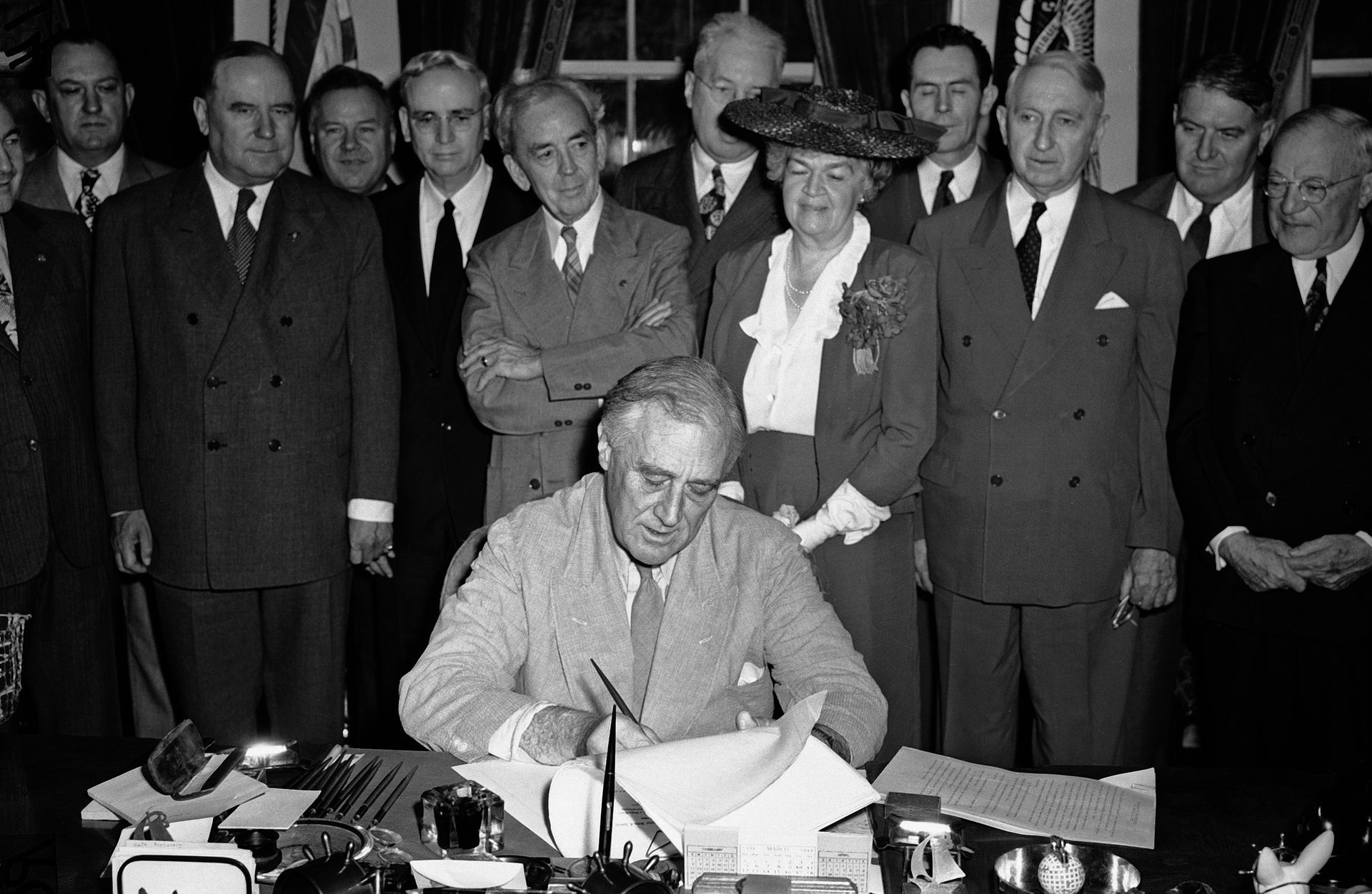 Man signing a document at a desk, surrounded by officials in a formal room