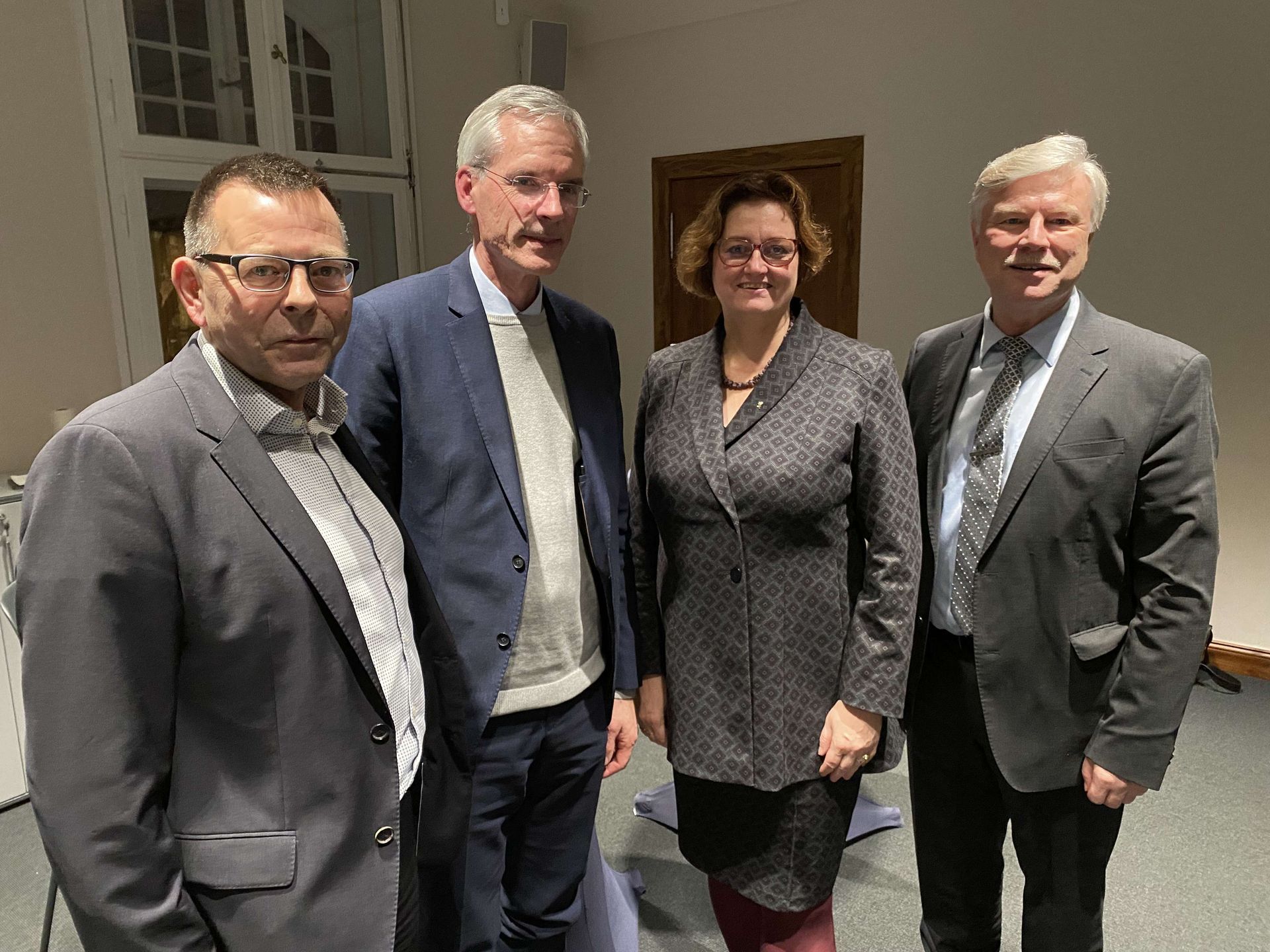 Drei Männer und eine Frau posieren in einem Raum für ein Foto.