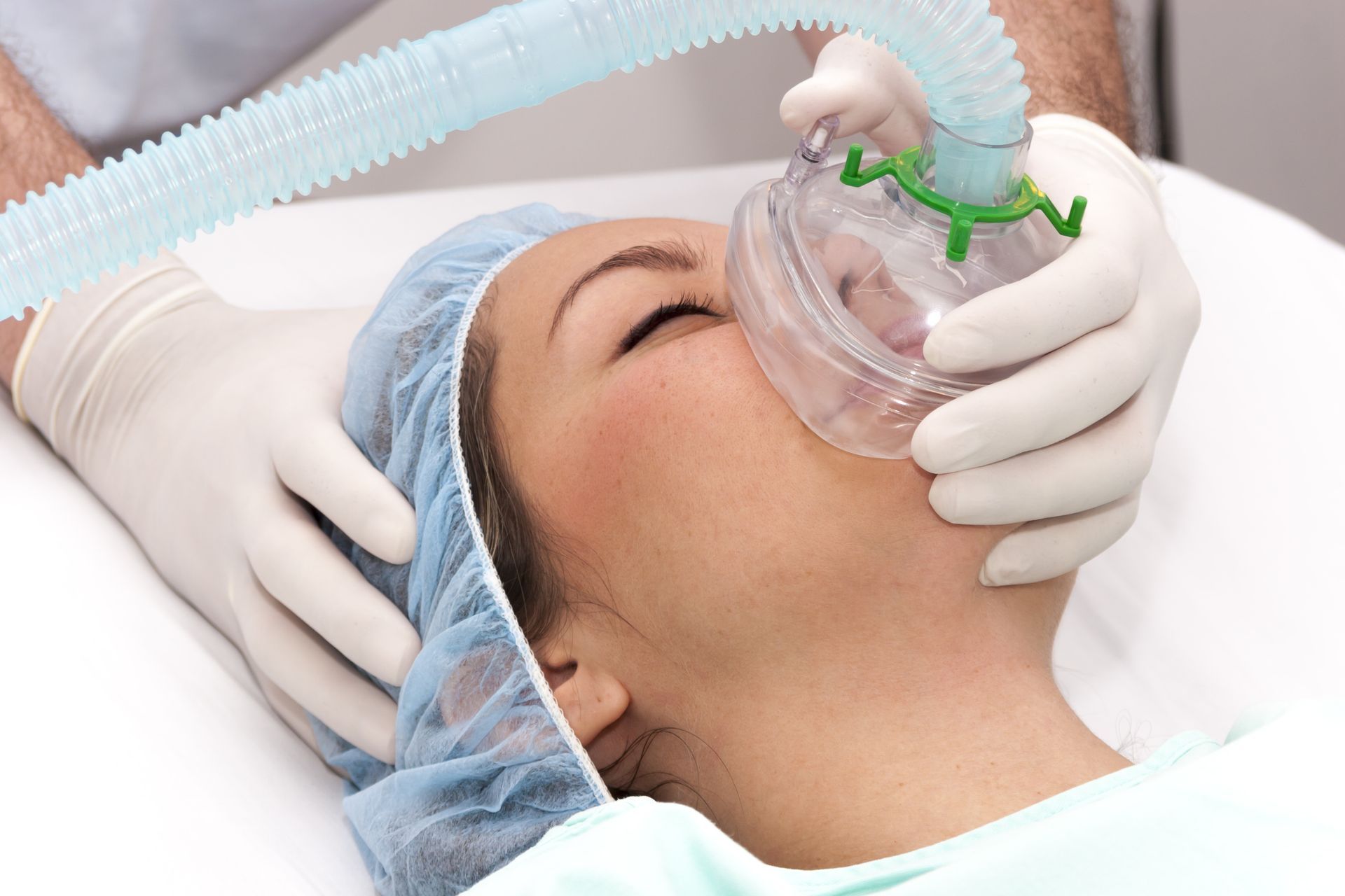 Eine Frau liegt mit einer Narkosemaske im Gesicht in einem Krankenhausbett.