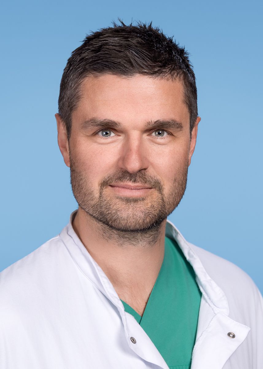 Eine Frau in einem weißen Laborkittel und mit Ohrringen lächelt in die Kamera.