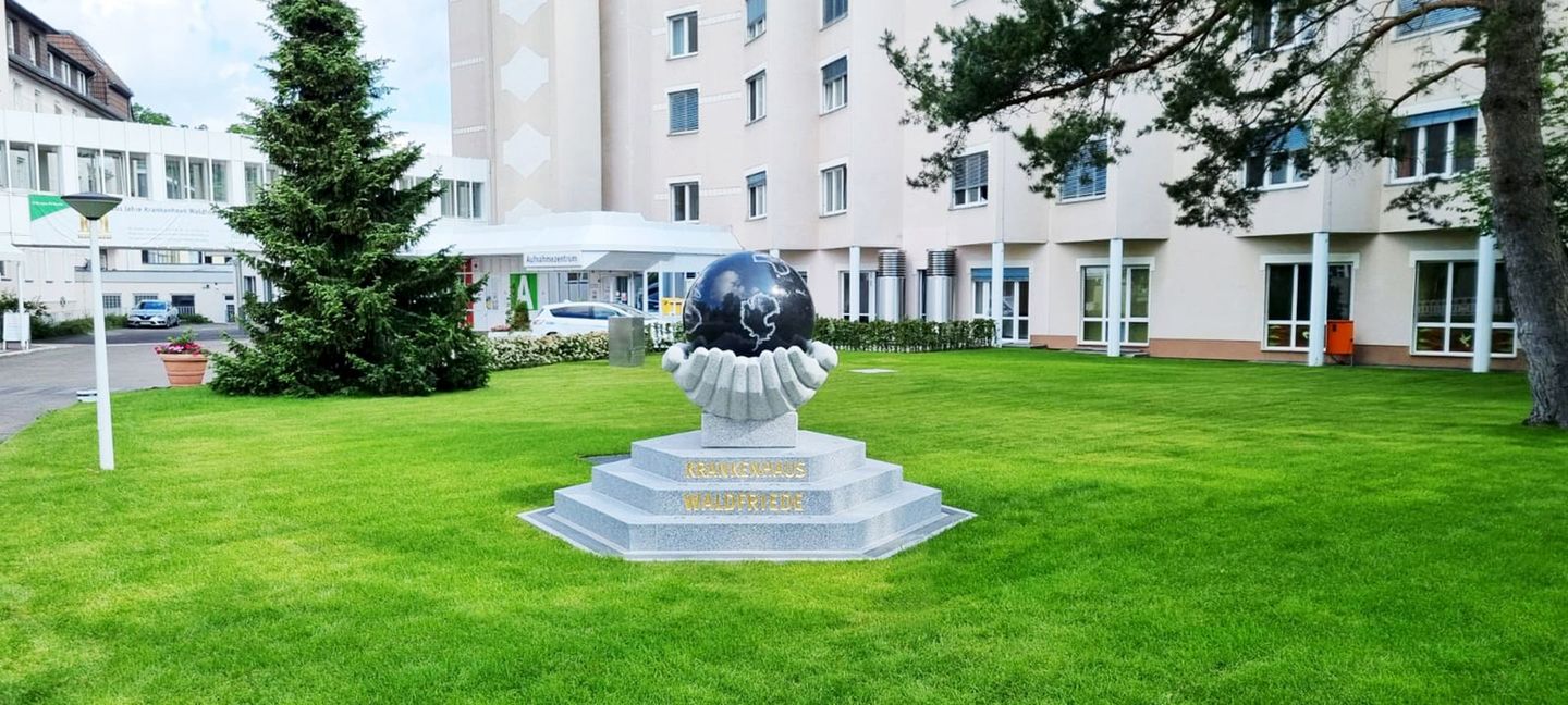 Eine Globusstatue in einer Vase in einem Park vor einem Gebäude.