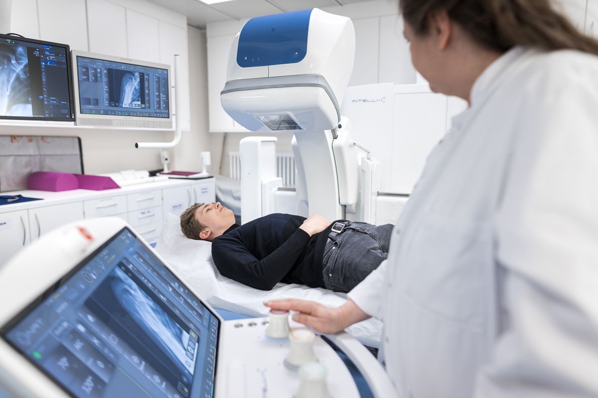 Eine Frau steht neben einem Mann, der in einem Krankenhausbett liegt.