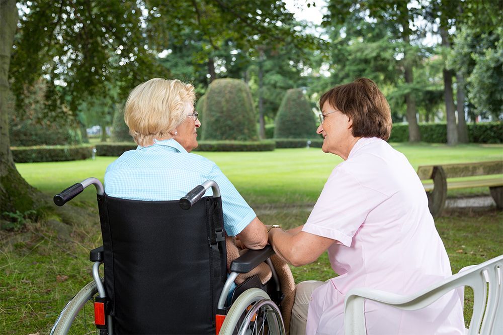 Eine Frau im Rollstuhl spricht in einem Park mit einer Krankenschwester.