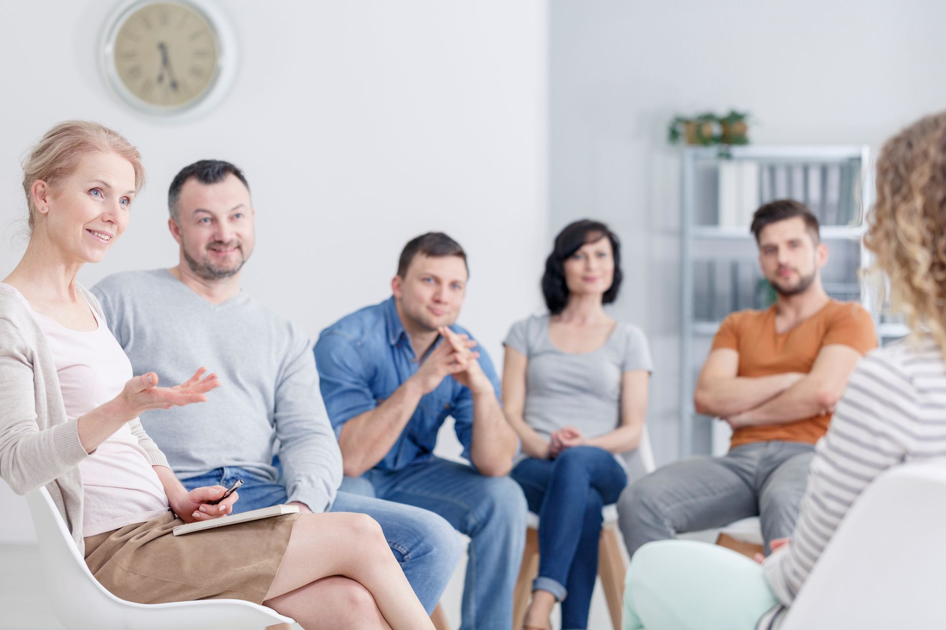 Gruppentherapiesitzung: Die Teilnehmer sitzen im Kreis und hören einer Frau zu, die spricht.