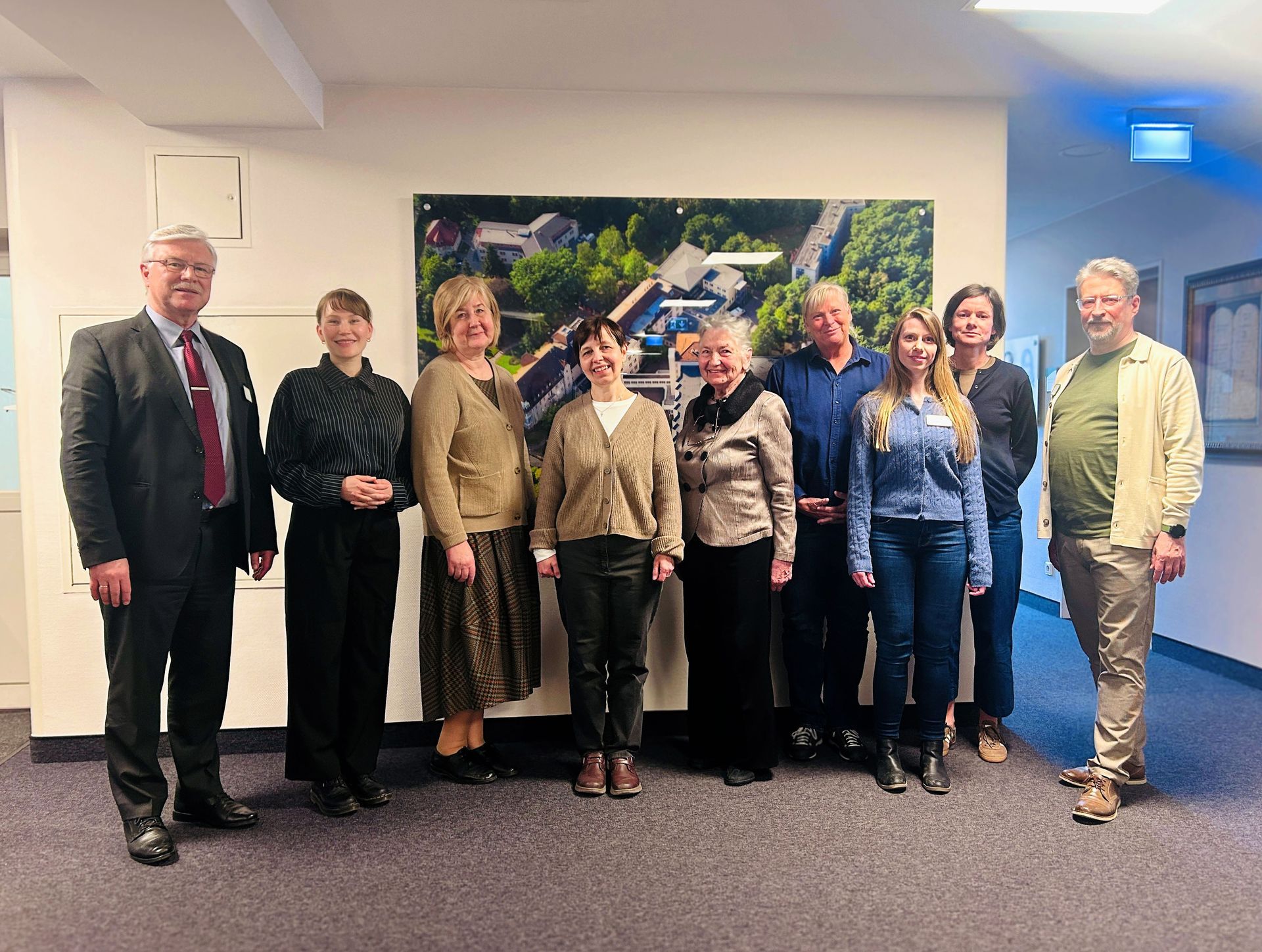 Acht Personen posieren in einem Konferenzraum vor einem Wandfoto.