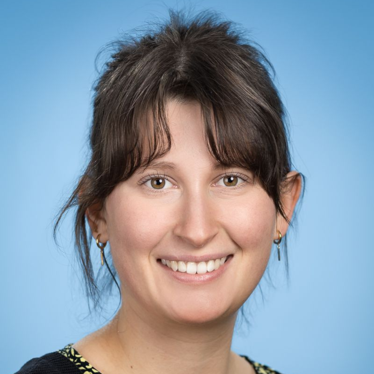 Eine Frau mit Brille und Ohrringen lächelt in die Kamera.