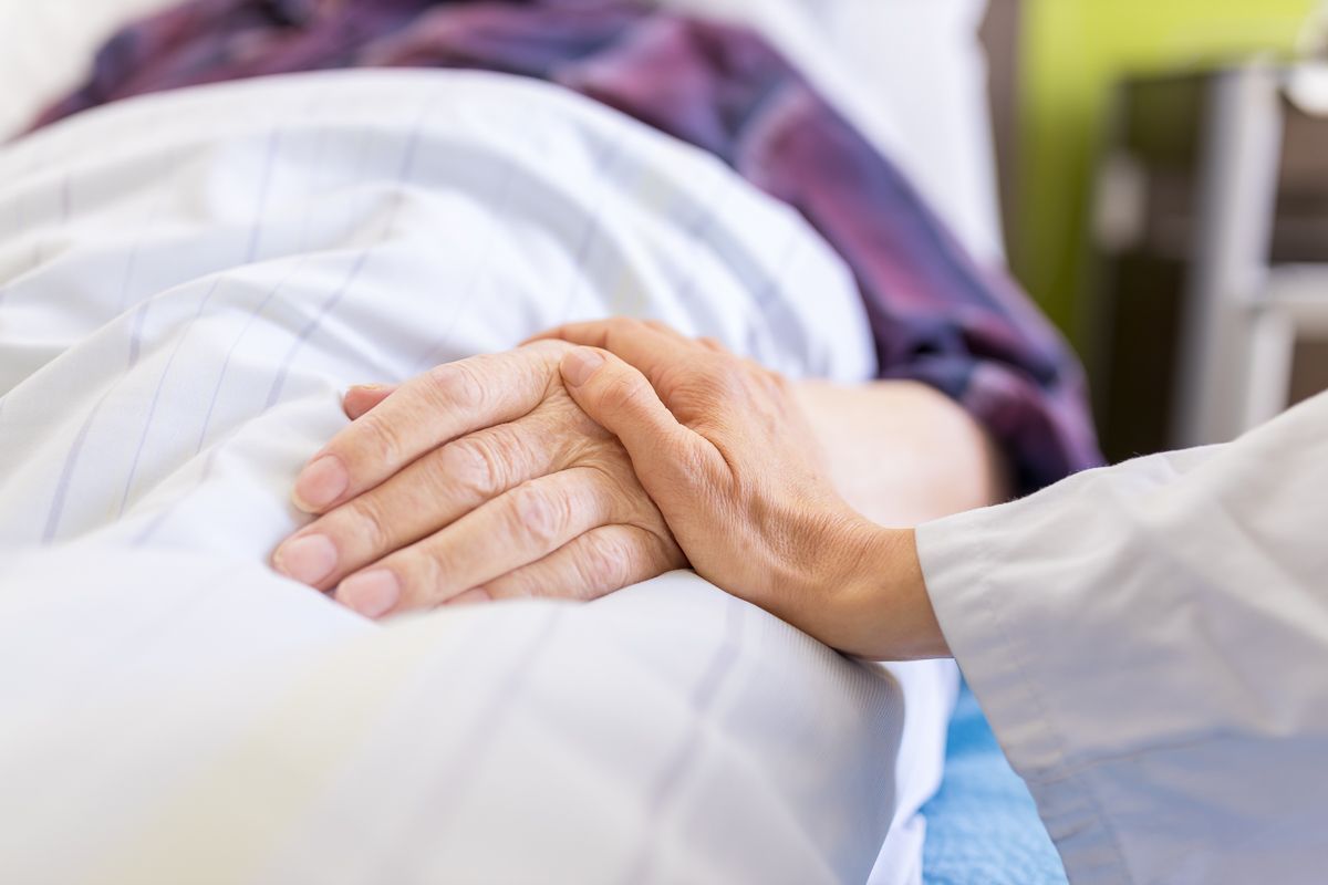 Ein Arzt hält die Hand eines Patienten in einem Krankenhausbett.