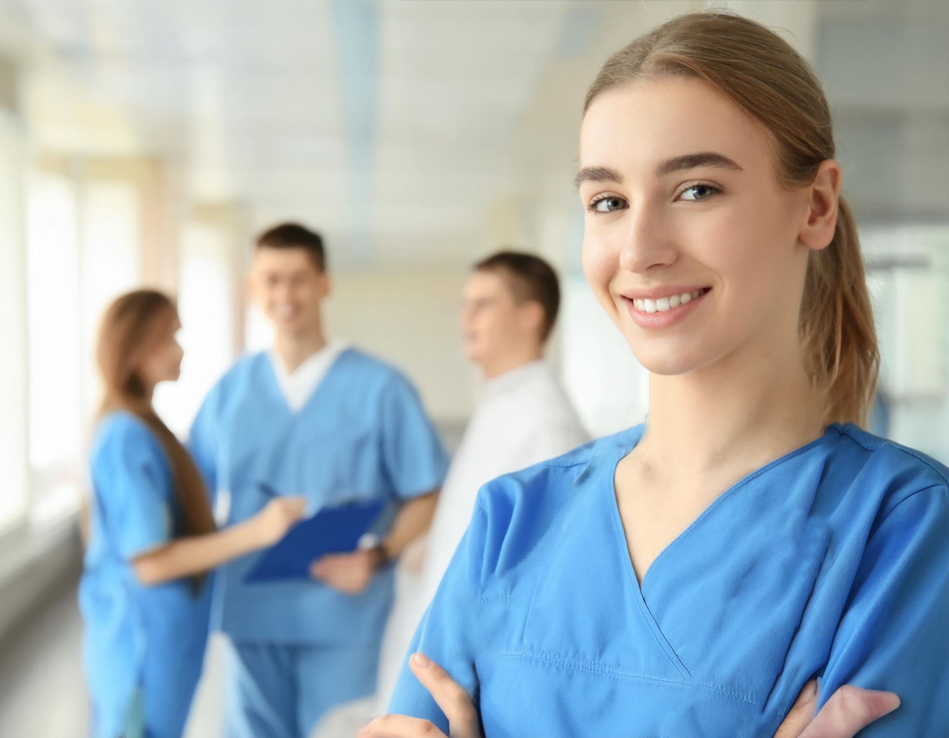 Eine Krankenschwester steht lächelnd und mit verschränkten Armen in einem Krankenhausflur.