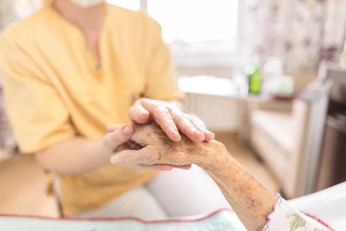 Eine Krankenschwester hält die Hand einer älteren Frau in einem Krankenhausbett.
